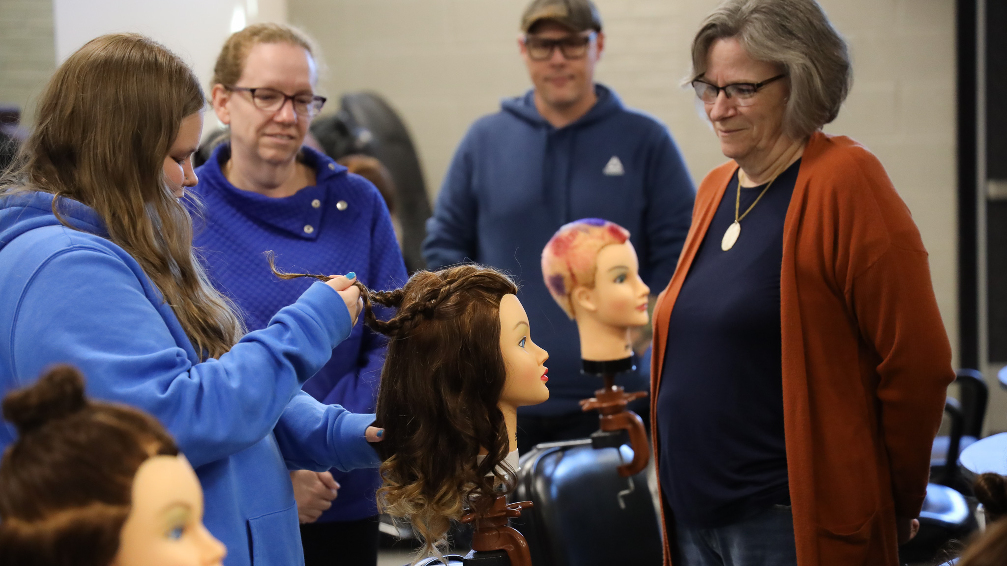 Cosmetology class practicing hair stying on mannequins while instructors watch