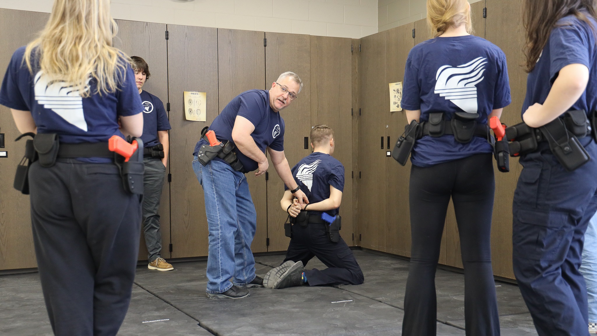 Four teen students watching as an instructor applies handcuffs to another student
