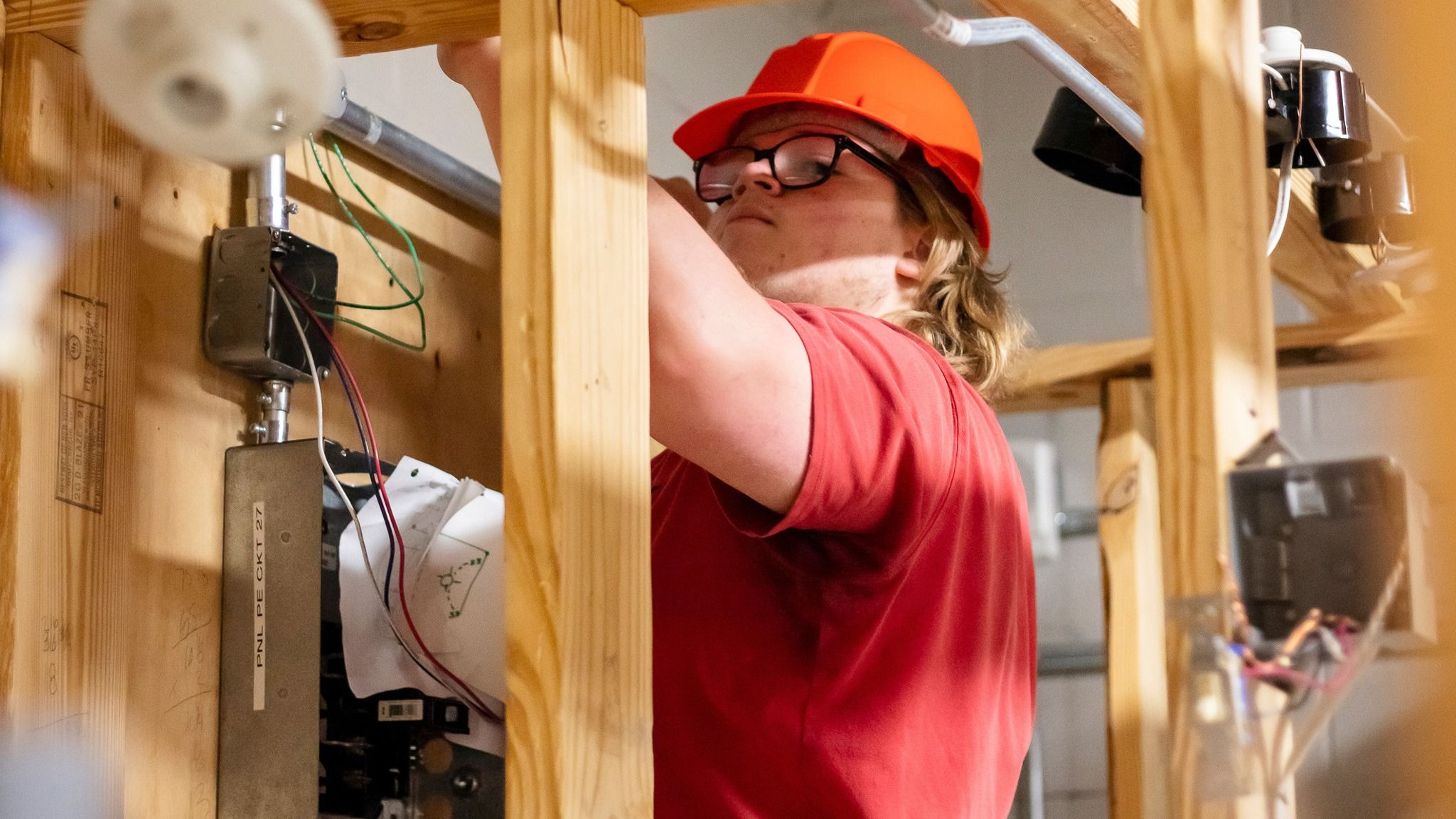 A teen student wearing a hardhat while installing an electrical light fixture