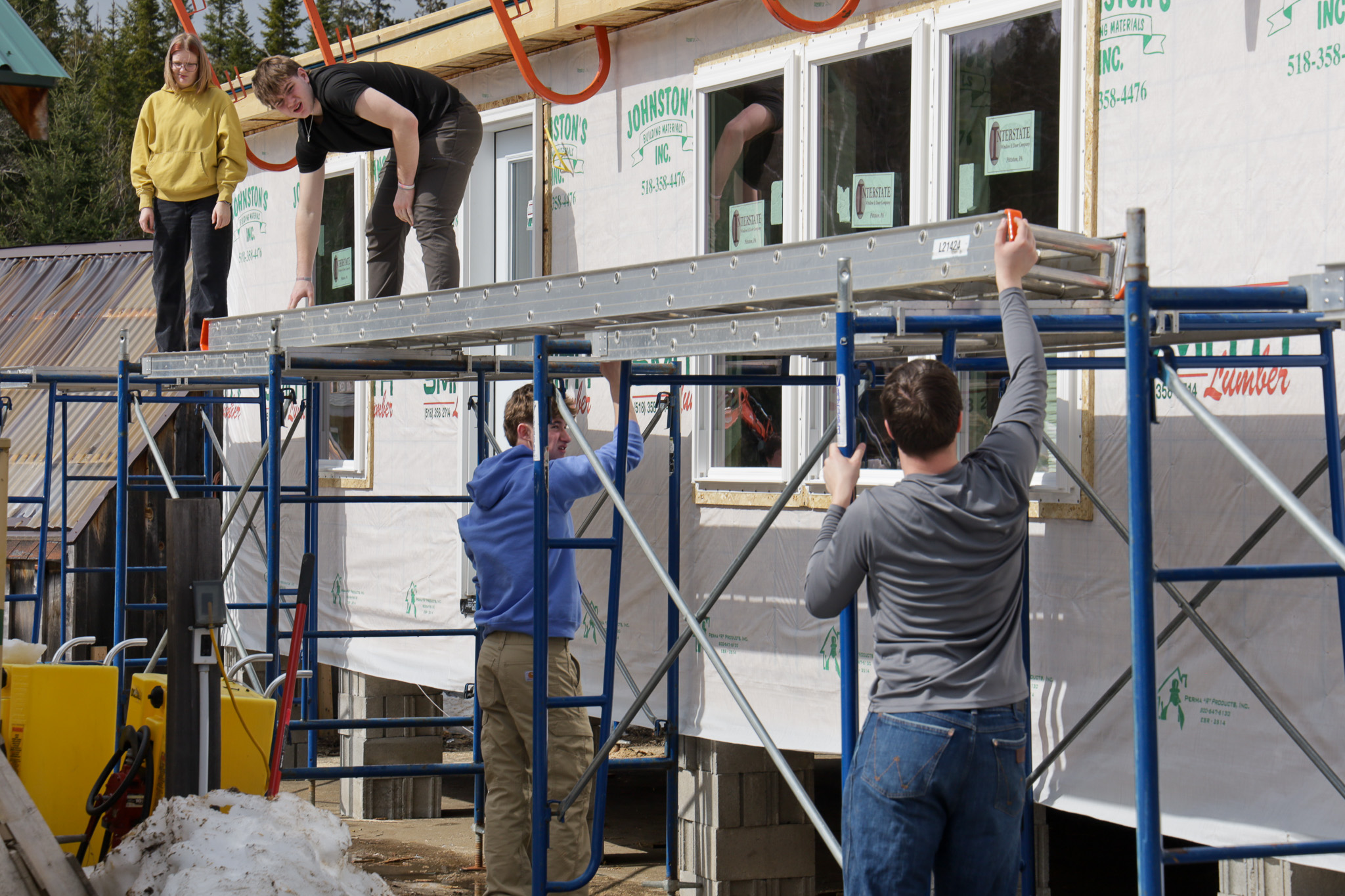 Two teen construction students working with power tools inside of a partially framed building