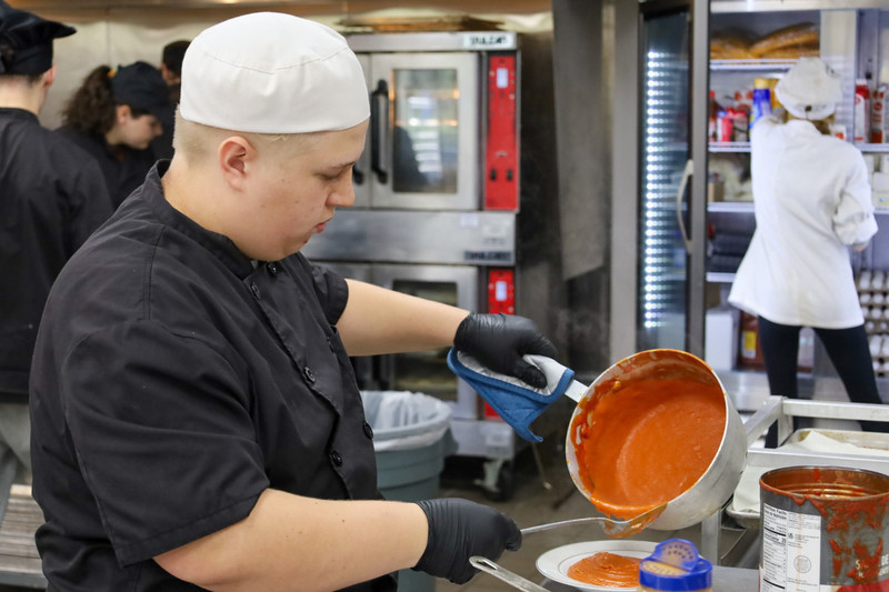 student pouring soup out of pan into bowl