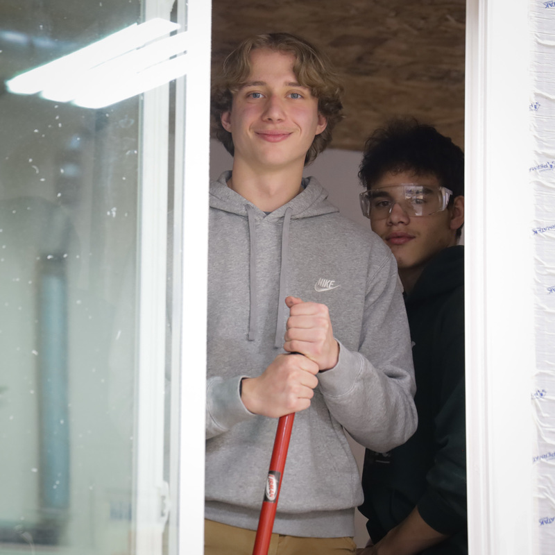 2 students smiling behind glass