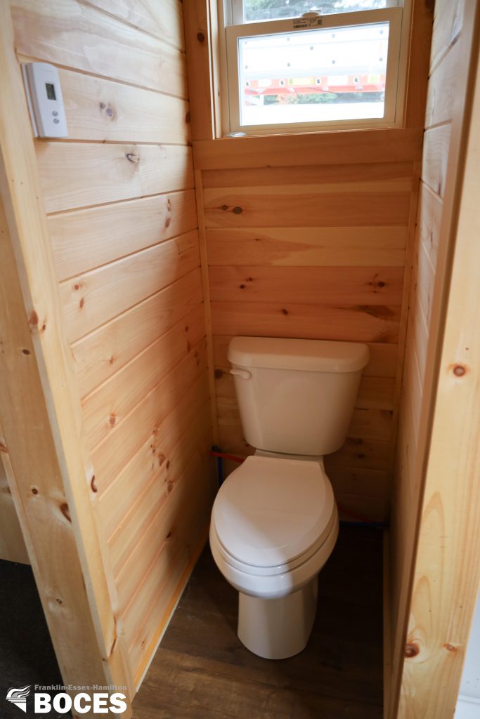 all pine interior of the tiny house, picture shows a toilet with a window high above it