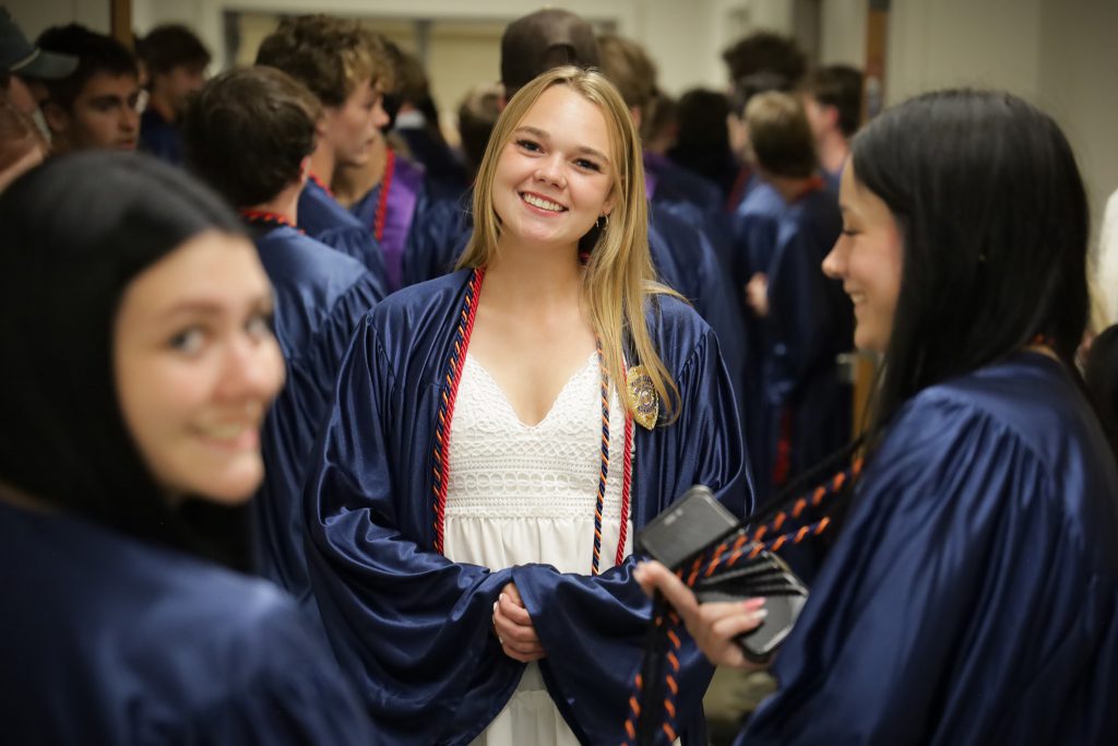 Graduates wait for ceremony to start in hallway. Graduates are smiling at camera